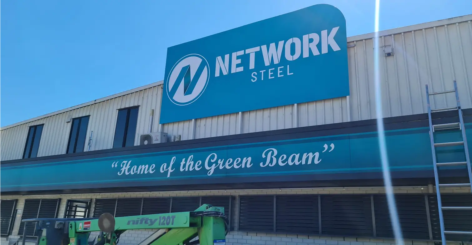 Large blue signage for Network Steel installed on the exterior facade of an industrial facility, representing heavy-duty commercial building signage.